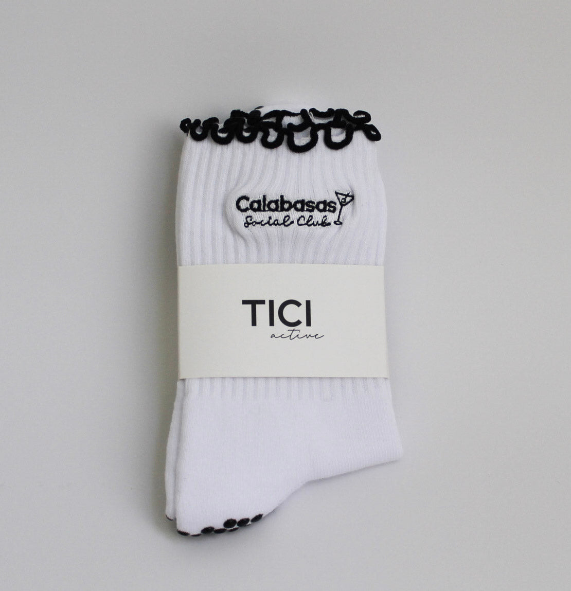 White socks with black accents and visible branding on a light gray background, tici active, calabasas social club grip socks for pilates