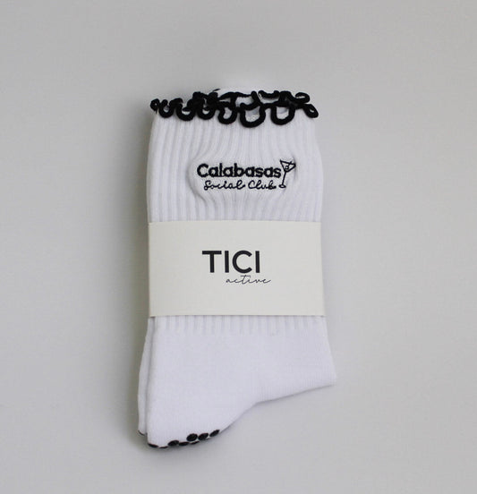 White socks with black accents and visible branding on a light gray background, tici active, calabasas social club grip socks for pilates 