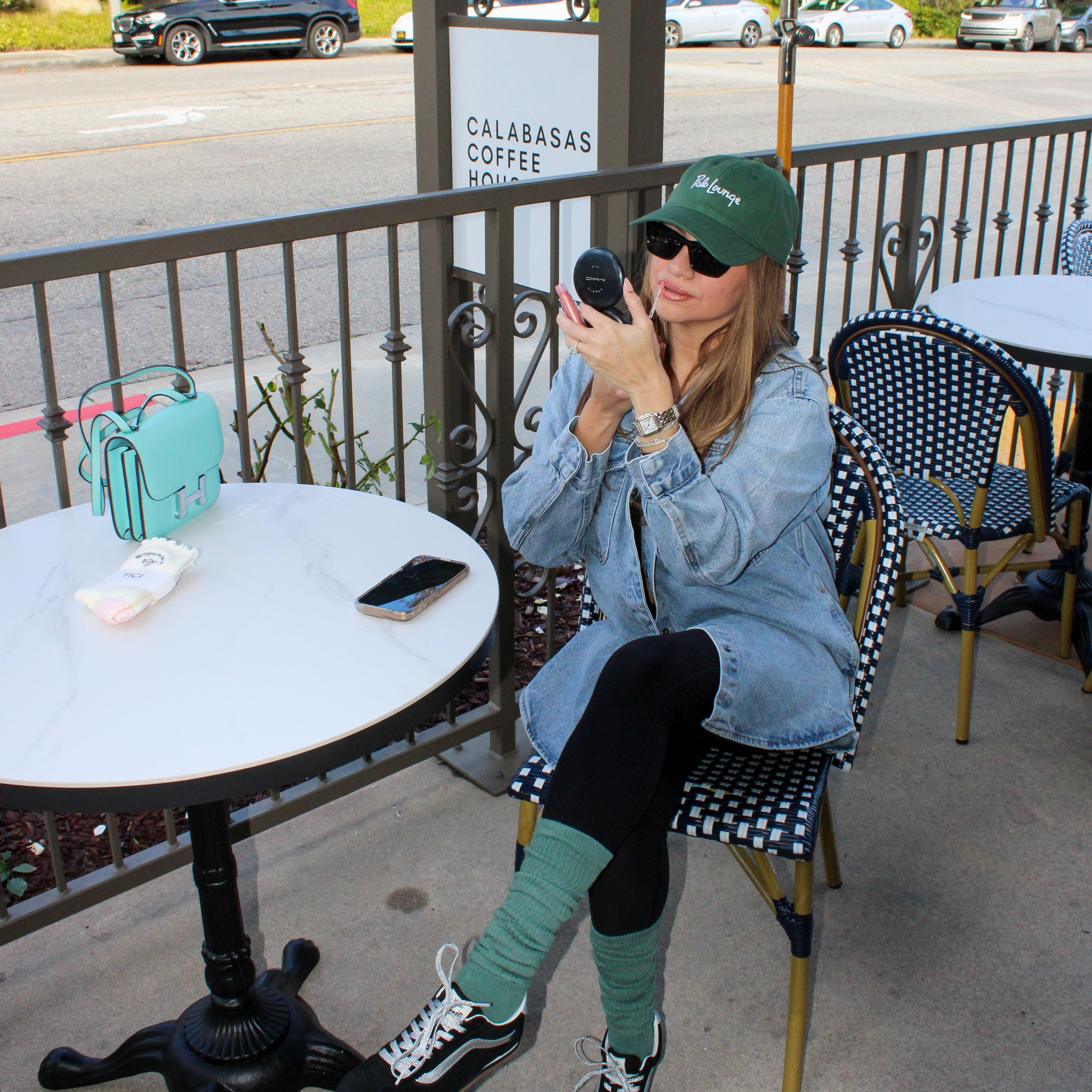 Person sitting at an outdoor cafe table applying makeup. Model is wearing tici active grip socks in the color matcha/green at calabasas coffee house. 