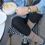 Person holding a cup of coffee outdoors, wearing a denim jacket and black leggings. Wearing tici active slouchy grip socks in the color latte/beige at calabasas coffee house.
