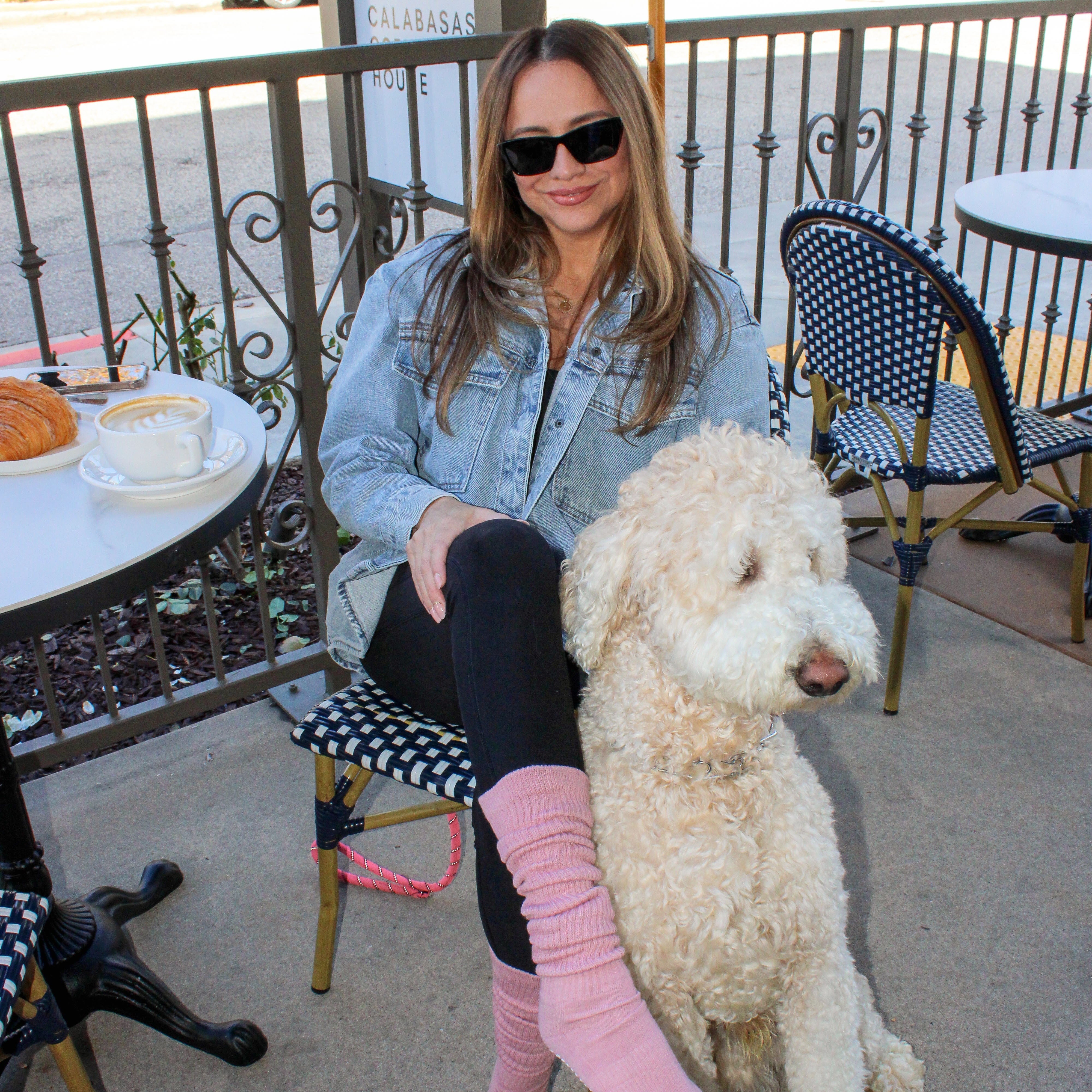 Woman with a dog on a patio with chairs and a table in the background wearing rose color tici active slouchy grip socks. Calabasas coffee house. 