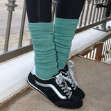 Person wearing black sneakers with white soles and green knee-high socks, standing on a concrete surface. tici active grip socks. matcha color. 