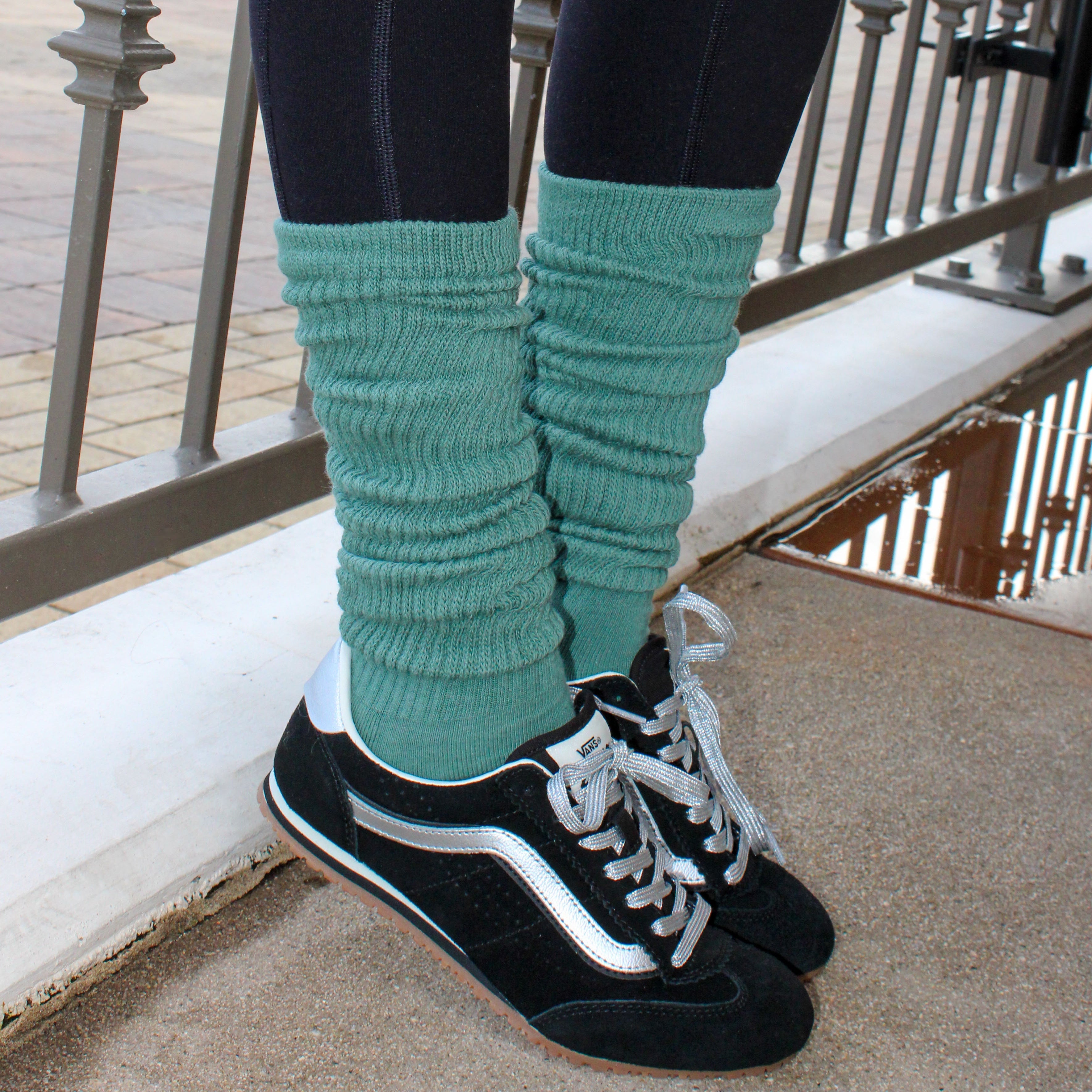 Person wearing black sneakers with white soles and green knee-high socks, standing on a concrete surface. tici active grip socks. matcha color. 