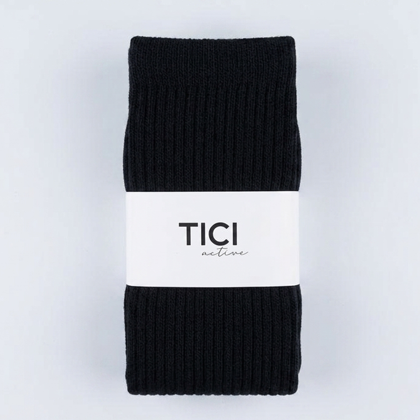 A pair of black ribbed knit pilates grip socks folded and wrapped with a white paper band printed with the brand name 'TICI ACTIVE'.