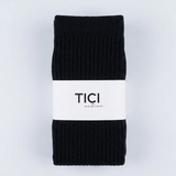 A pair of black ribbed knit pilates grip socks folded and wrapped with a white paper band printed with the brand name 'TICI ACTIVE'.