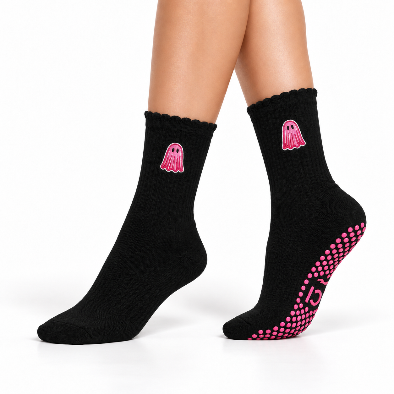 A pair of black crew socks worn on a model's feet, featuring a pink ghost graphic on the side and pink grip dots on the sole, against a plain white background.