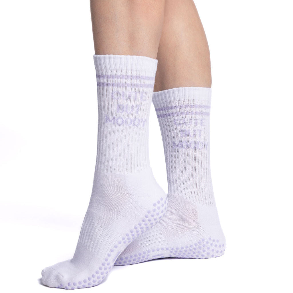 White pilates socks with lavender grips with text that reads, CUTE BUT MOODY worn by a person on a white background
