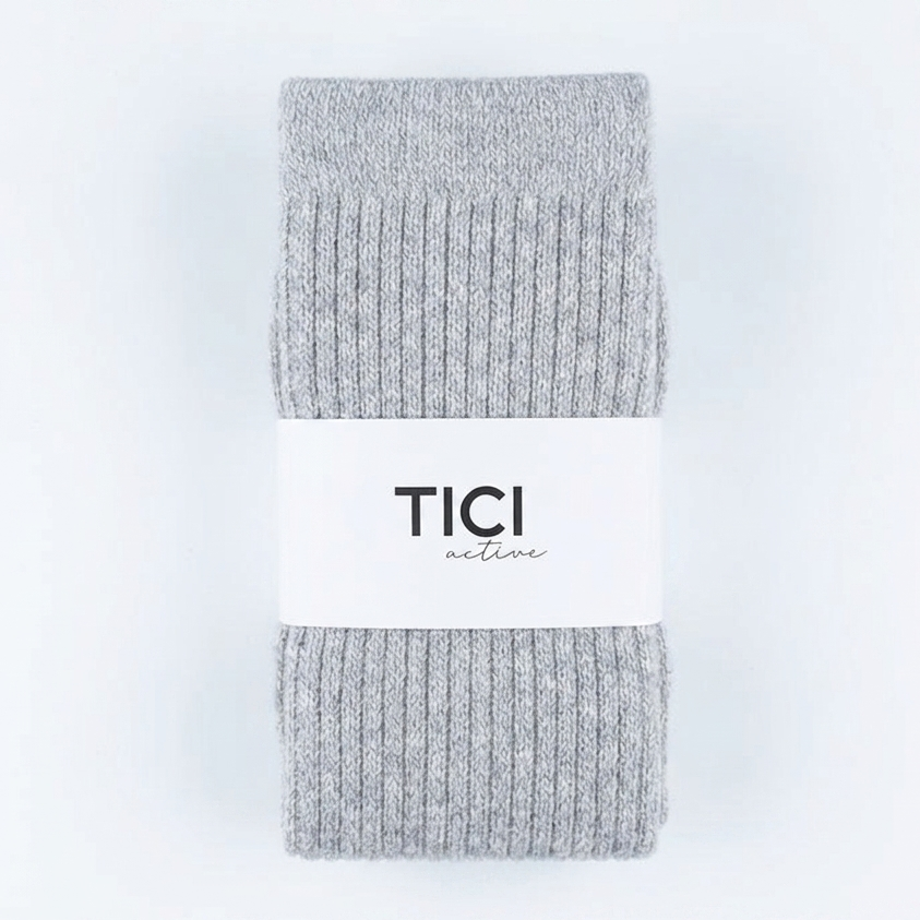 A pair of light gray ribbed knit socks folded vertically with a white paper band around the middle that reads 'TICI nature' in black text, set against a plain white background.