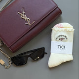 Maroon YSL handbag, YSL sunglasses, and a cream TICI ACTIVE socks with pink jet with the text "no labeled 'TICI' on a gray surface.crying on the pj"