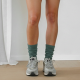 Person wearing green socks and gray sneakers standing on a neutral background