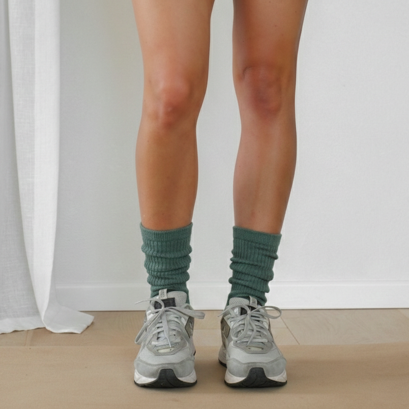 Person wearing green socks and gray sneakers standing on a neutral background