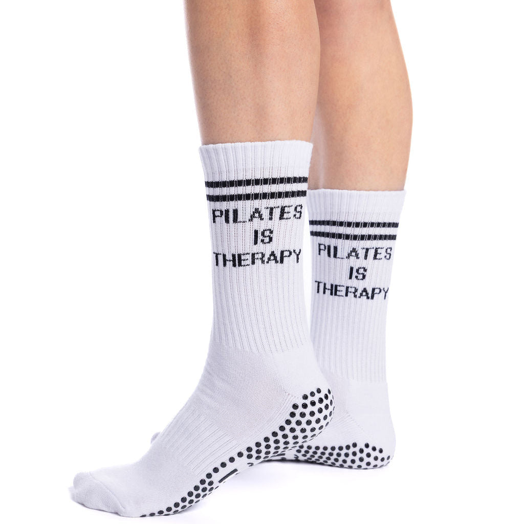 White pilates socks with black grips with 'Pilates is Therapy' text worn by a person on a white background