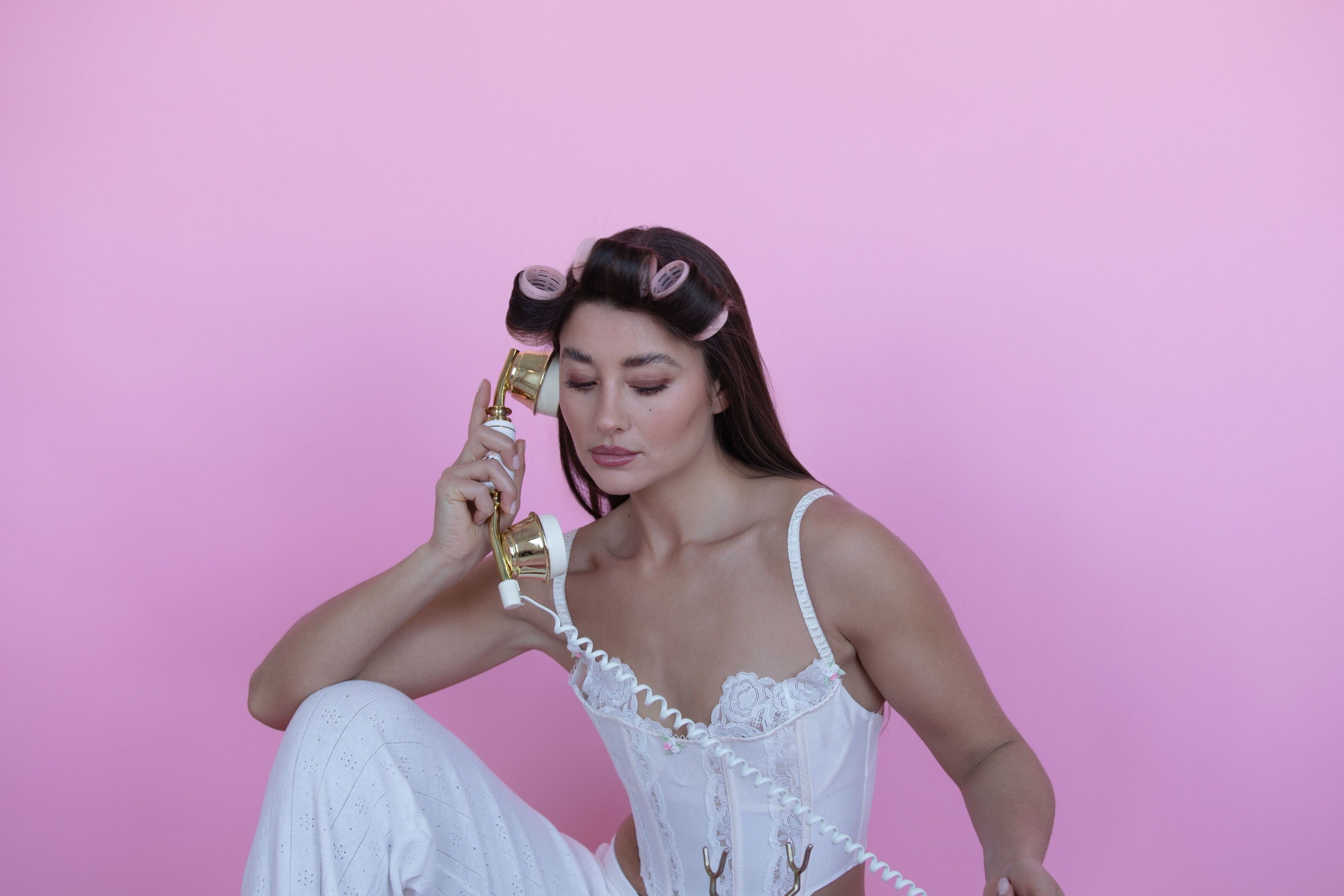 Woman with hair in rollers holding a gold phone on a pink background. campaign for tici active valentines day