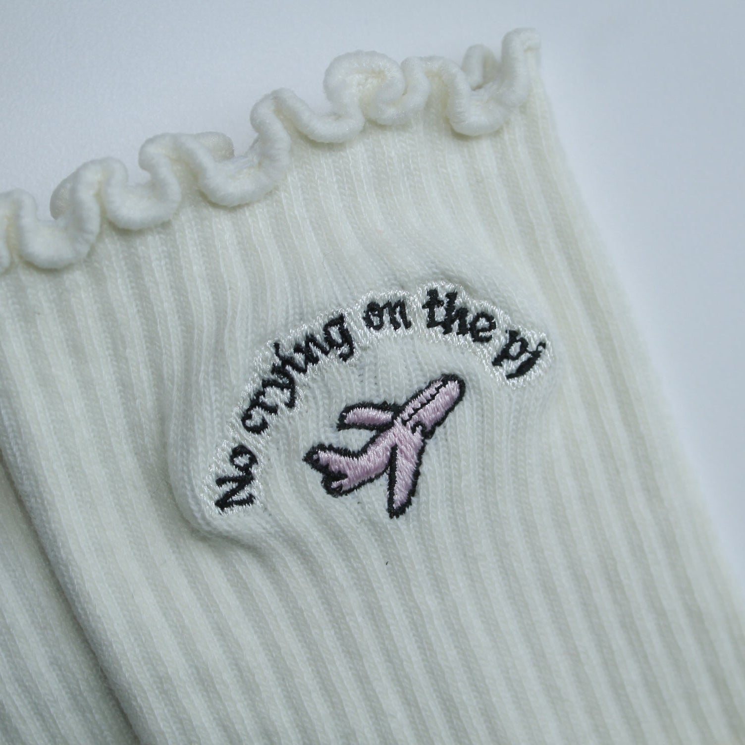 Pair of grip socks with a TICI active label on a light pair of cream socks and a pink jet. no crying on the pj in black embroidery text. lettuce edge ruffle. 