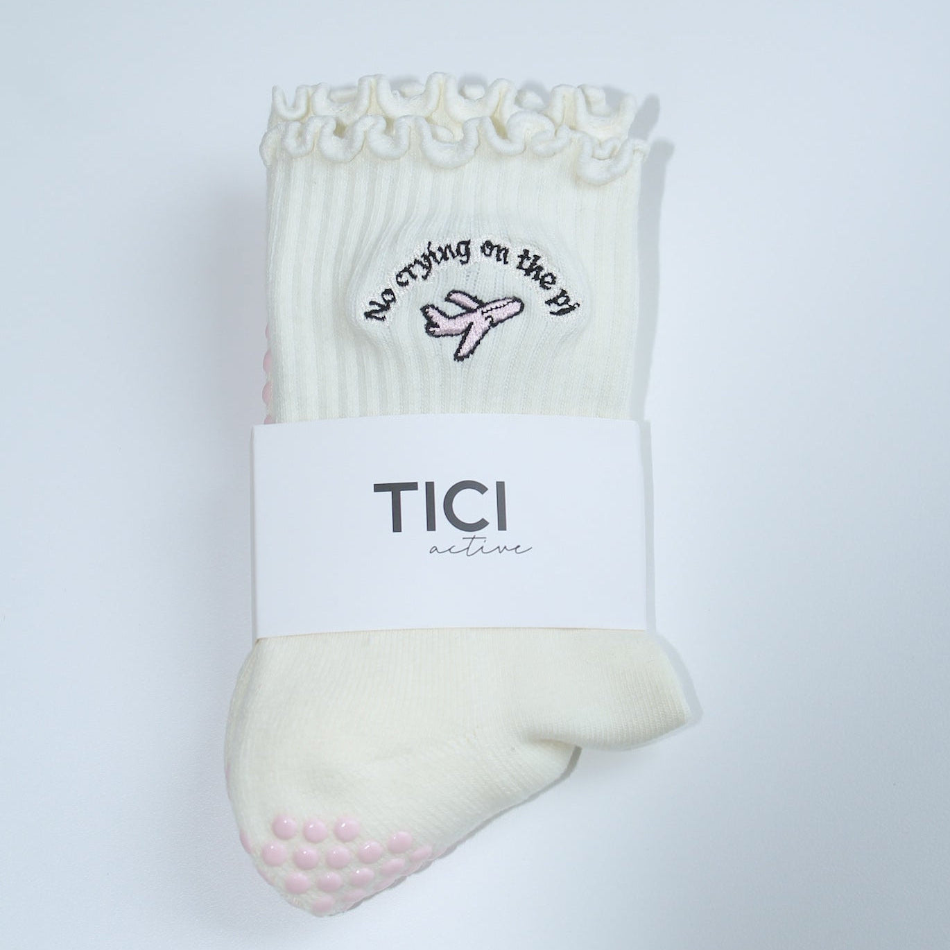 Pair of grip socks with a TICI active label on a light pair of cream socks and a pink jet. no crying on the pj in black embroidery text.
