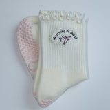 Pair of grip socks with a TICI active label on a light pair of cream socks and a pink jet. no crying on the pj on black embroidery text