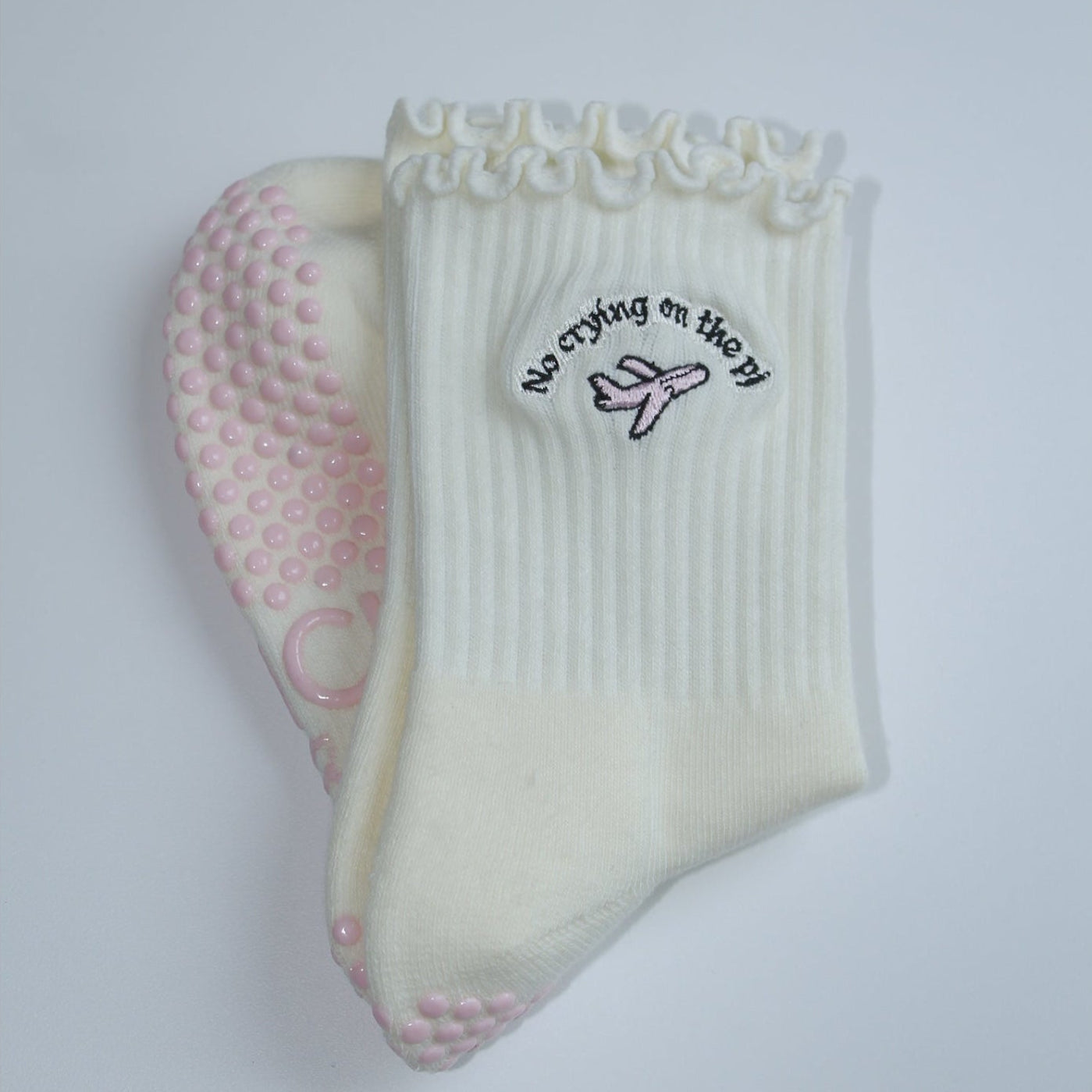 Pair of grip socks with a TICI active label on a light pair of cream socks and a pink jet. no crying on the pj on black embroidery text