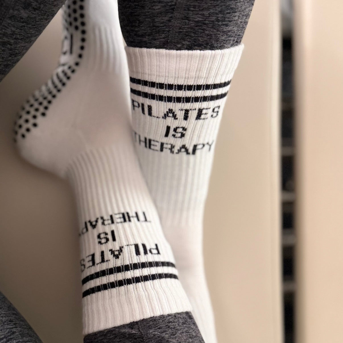 White pilates grip sock with 'Pilates is Therapy' text worn by a person sitting on a pilates reformer