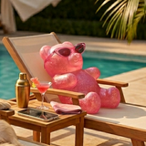 Pink gummy bear on a poolside chair with TICI ACTIVE product, pool and cabana in the background. Pilates socks .