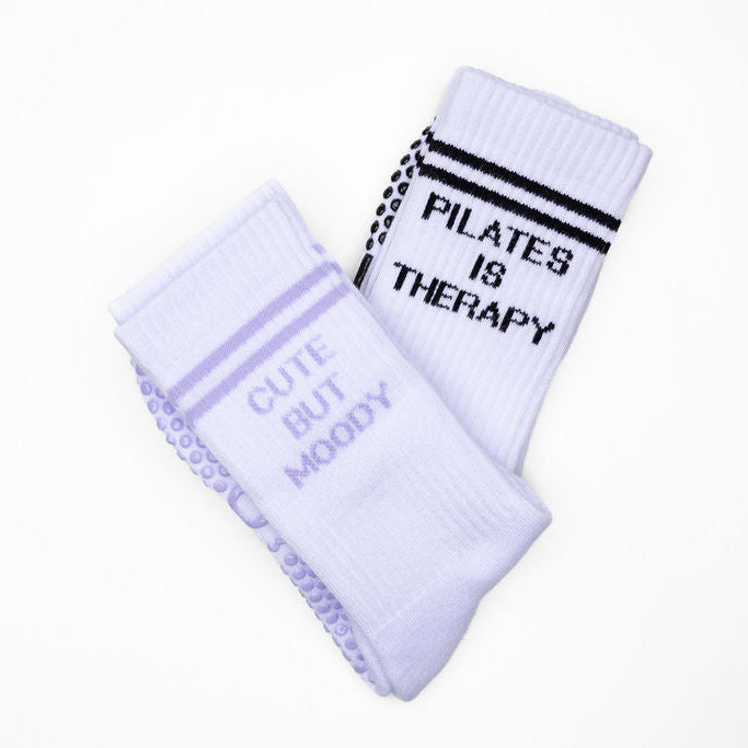 Two pairs of socks with text on a white background. pilates is therapy and cute but moody. pilates grgip socks.